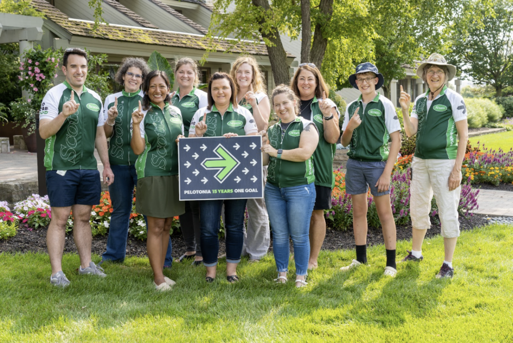 Image of a group of people wearing bike riding kits with Pelotonia logos and a Pelotonia sign